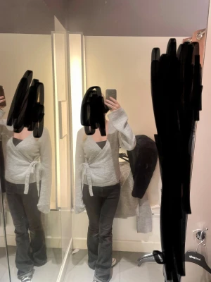 Grå omlottkofta med knyt - Säljer en ljusgrå omlottkofta från Gina Tricot med långa ärmar och knyt i sidan. Koftan är stickad och har en mjuk, cozy vibe som passar perfekt till jeans eller leggings. Snygg v-ringad design som ger en chill och trendig look.