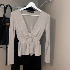 Party topp - Snygg beige topp från BikBok med lång ärm och v-ringning. Toppen har en knytdetalj framtill och en lätt volang vid midjan. 