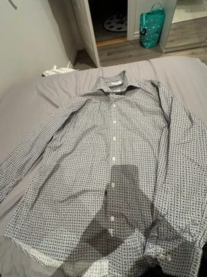 Mönstrad skjorta från Eton, strl 44 - Säljer en snygg långärmad skjorta från Eton i storlek 44 med ett unikt blått och vitt geometriskt mönster. Skjortan har klassisk krage, vita knappar och är tillverkad i bomull. Perfekt för dig som vill sticka ut lite extra.