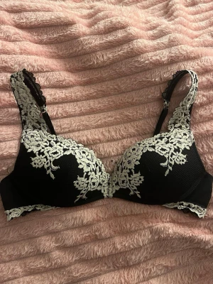 Svart bh från Intimissimi 🖤 - Snygg svart bh från Intimissimi med dekorativ vit spets längs axelbanden och kuporna. 😍 Bh:n har justerbara axelband. Säljer då den är för stor för mig 🥰Nästan helt ny, använd väldigt få gånger!Priset kan diskuteras, nuvarande priset beror på hur pass ny bh:n är ❤️