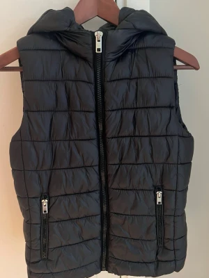 Svart dunväst från Mango Basics - Säljer en svart quiltad dunväst från Mango Basics med huva. Bra sick 