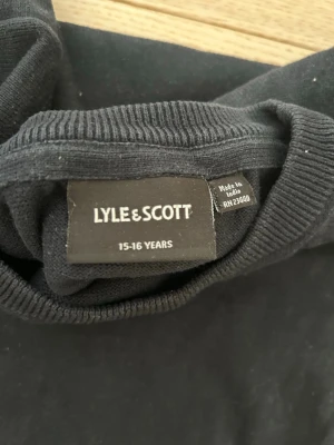 Mörkblåtröja från Lyle & Scott - Säljer en svart tröja från Lyle & Scott i klassisk modell. Tröjan har rund halsringning och ribbade muddar vid ärmslut.