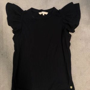 Svart topp med volangärm Pernilla Wahlgren - Söt svart topp från Pernilla Wahlgren med volangärmar. Toppen är ribbad och är i storlek xs. Använd två gånger, säljer pga att den inte kommer till användning. Hör av dig för frågor!💗