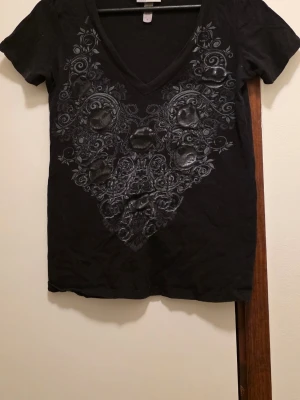 Jack Skellington, Nightmare Before Christmas, Disney - Cool svart t-shirt från Disneyland Resort med v-ringning och detaljerat döskallemönster framtill i grått och silver. T-shirten har korta ärmar och är gjord i mjuk bomull. Perfekt för dig som gillar edgy och unika prints. Köpt på Disneyland i Los Angeles. Står M men är mer dom en L.