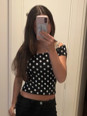 Svart prickig topp - Säljer en svart croppad topp med vita prickar. Toppen har en tight passform och korta ärmar som sitter lite offshoulder. Materialet känns mjukt och stretchigt, perfekt till sommaren. Superfin att styla med höga jeans eller kjol!