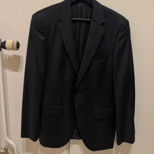 Svart Loro Piana kavaj från Boss - Snygg svart kavaj från Boss, Super 150 Loro Piana Luxury Choice, tillverkad i Italien. Klassisk modell med två knappar, fickor med lock och bröstficka. Tidlös design i exklusiv ull som känns lyxig och passar perfekt till alla tillfällen där du vill vara extra stilig.   Kavajen i färgen Svart, köptes ny i butik för cirka 12000kr och har enbart används vid ett fåtal tillfälle.