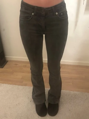 Svarta bootcut jeans - Säljer ett par gråa bootcut jeans med klassisk femficksmodell och hällor för bälte. Jeansen har en tight passform upptill och lätt utsvängda ben. Materialet är jeans och färgen är mörk grå. Perfekta för dig som gillar en tidlös och snygg look.