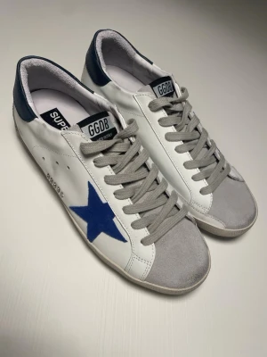 Golden Goose Skor - Snygga sneakers från Golden Goose med den ikoniska mörkblåa stjärnan. Skorna är i bra skick och kommer med dustbag. Modellen heter Superstar och skorna är storlek 42. Pris kan diskuteras 🤝 Skriv ifall ni har fler frågor 💯