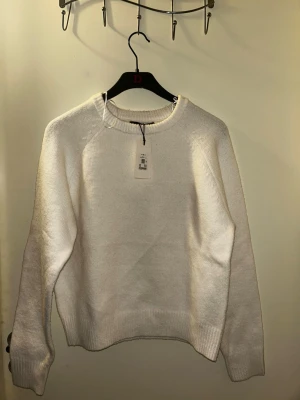 Vit stickad tröja från Bik Bok - Klassisk vit stickad tröja från Bik Bok i storlek M. Tröjan har rund halsringning, ribbade muddar och en enkel, clean look som passar till allt. Perfekt för lager på lager under kyliga dagar.