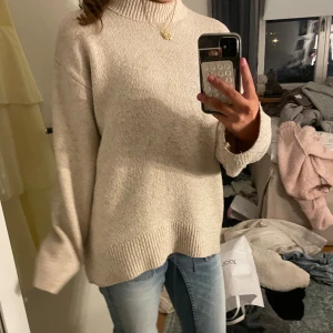 Beige stickad polotröja oversized - Mysig beige stickad polotröja med oversized passform och långa ärmar. Tröjan har bred ribbad kant vid ärmslut och nederkant samt hög polokrage. Perfekt för kyliga dagar och enkel att styla med jeans eller kjol.