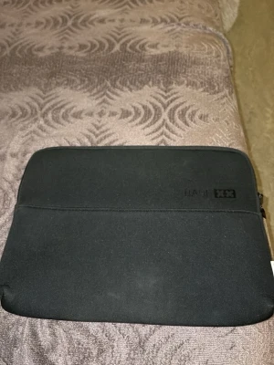 Svart BASE XX datorväska - Slimmad svart datorväska från BASE XX med enkel design och dragkedja. Perfekt för att skydda din laptop på språng. Väskan är tillverkad i ett mjukt syntetmaterial och har en diskret logga på framsidan.