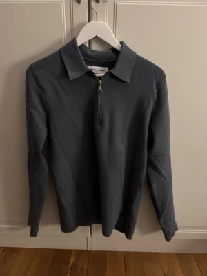 Mörkgrå långärmad tröja med half zip - Säljer en stilren mörkgrå långärmad tröja från samøe samsøe. Tröjan har klassisk krage och en snygg half zip-dragkedja framtill. Perfekt till jeans eller chinos för en clean look. Materialet känns mjukt och bekvämt mot huden.