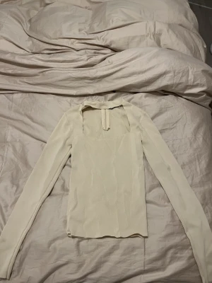 Beige långärmad topp från ZARA - Säljer en stilren beige långärmad topp från ZARA i storlek S. Toppen har fyrkantig ringning framtill och dragkedja i ryggen. Tillverkad i ett mjukt, lätt strukturerat material som känns skönt mot huden. Perfekt att styla med jeans eller kjol.