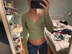 Ljusgrön croppad ribbad kofta - Säljer en ljusgrön croppad kofta med ribbad struktur och v-ringning. Tröjan har långa ärmar och knappar framtill, perfekt för dig som gillar en trendig och enkel stil. Passar snyggt till både jeans och kjol!