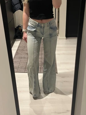 Ljusblå wide jeans med cargofickor - Säljer ett par ljusblå jeans med breda ben och fina fickor framtill. Jeansen har låg midja och fina tydliga sömmar längs benen. Använda ett fåtal gånger, de är i väldigt bra skick.