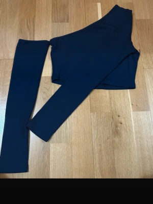 Mörkblå oneshoulder topp från SHEIN - Säljer en mörkblå croppad topp från SHEIN med oneshoulder-design och lång ärm. Toppen är ribbad och tillverkad i stretchigt material som består av polyester och elastan. Perfekt för dig som vill ha en stilren och trendig look.