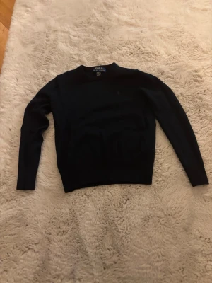 Svart tröja från Polo Ralph Lauren cashmere - En klassisk svart långärmad tröja från Polo Ralph Lauren. Tröjan har rund halsringning och är tillverkad i ett mjukt material som passar perfekt till kyligare dagar. Enkel och stilren design som funkar till det mesta.