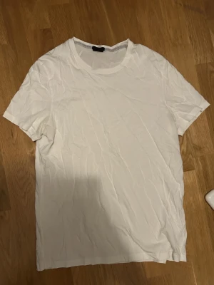 Vit slim fit t-shirt från Hugo Boss - Säljer en stilren vit t-shirt från Hugo Boss i slim fit-modell. Tröjan har rund halsringning och korta ärmar. Tillverkad i mjuk bomull som känns skön mot huden. Perfekt basplagg för en clean och enkel look.