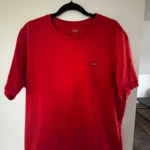 Röd t-shirt från Levi's - Klassisk röd t-shirt från Levi's med liten logga på bröstet. T-shirten har rund halsringning och korta ärmar. Tillverkad i mjuk bomull som känns skön mot huden. Perfekt till jeans eller shorts för en enkel och clean look.