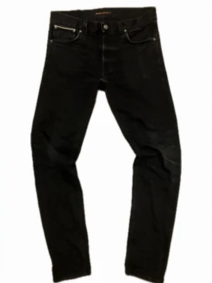 Svarta Nudie Jeans Selvedge - Säljer ett par svarta jeans från Nudie Jeans med selvedge-detalj. Klassisk femficksmodell med silverfärgade nitar och knapp. Jeansen har en tight passform och är tillverkade i slitstarkt jeansmaterial. Perfekta för dig som gillar stilrena och tidlösa plagg. Tveka inte på att höra av dig vid frågor!