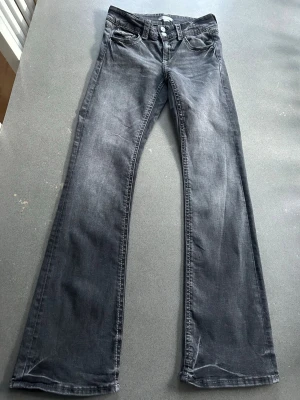 Mörkgrå lågmidjade utsvängda jeans Gina 170 - Fint skick utan slitage. Storlek 170, passar XS. En liten ”fläck” bak på ena benet, knappt synbar.  Låg midja, low waist, boot cut.  Tvättar utan sköljmedel och torktumlar inte kläder.