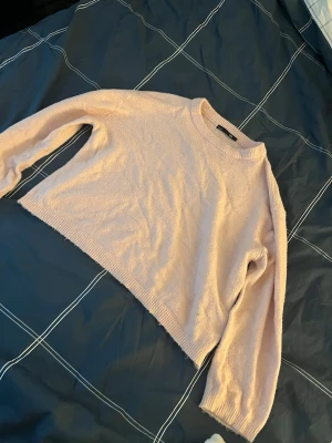 Ljusrosa stickad tröja från 157 - Mysig rosa stickad tröja från 157 med rund halsringning och ribbade muddar vid ärmslut och nederkant. Lite kortare och tunnare i modellen. Noppror förekommer.