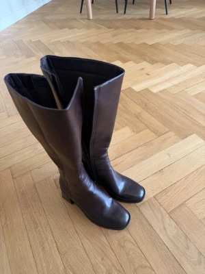 Bruna höga skinnstövlar - Säljer ett par stilrena bruna stövlar i skinn med fyrkantig tå och bred låg klack. De är knähöga!
