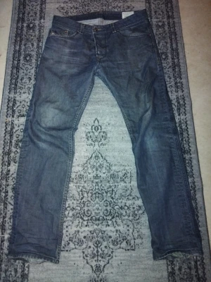 Diesel Darron jeans blå tapered 32/32 - Säljer ett par blå Diesel Darron jeans i regular slim-tapered modell. Klassisk femficksdesign, snygga slitningar och detaljerade sömmar på bakfickorna. Jeansen är i ett mjukt denimtyg och har en något smalare passform nedtill.