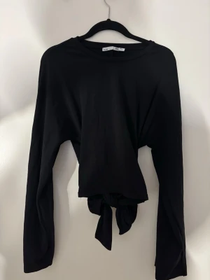 Svart croppad långärmad topp med knyt - Säljer en svart croppad långärmad topp från lager157. Toppen har en enkel rund halsringning och en snygg knytning framtill som ger en cool twist. Har endast använt en gång i ca 4 timmar 