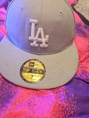 Grå New Era 59FIFTY LA keps - Säljer en stilren grå New Era 59FIFTY keps med LA-logga framtill och broderade detaljer. Klassisk rak skärm och broderad MLB-logga bak. Perfekt för dig som gillar streetwear och sportig stil.