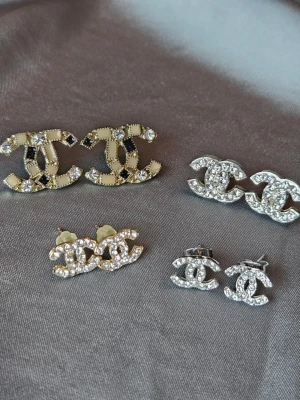 4 par örhängen med CC-motiv - 4 par örhängen med CC-motiv. Små i guldfärg är inte använda men de andra är i använt skick. De beige/guldiga har tappat lite färg på baksidan. Mått: Små silvriga 10x8mm Små guldiga 12x8mm Stora silvriga 14x11 mm Stora guldiga 20x15mm  Se bilder för egen bedömning.