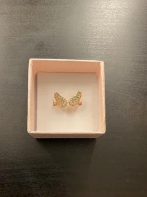 Guld ring  - Guldig ring med ängelvingar som aldrig använts. Ringen går att spänna ut och in till den storlek som önskas. Ringen är inte äkta guld. 