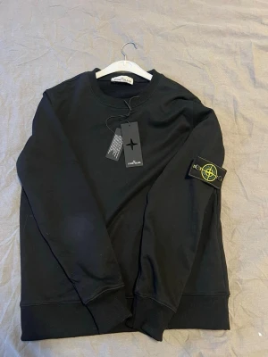 Svart sweatshirt från Stone Island - Säljer en svart sweatshirt från Stone Island med den ikoniska patchen på ärmen. Tröjan har rund hals, ribbade muddar och är tillverkad i mjuk bomull. Perfekt för dig som vill ha en clean och stilren look med streetwear-vibe. Använt fåtal gånger. Pris går att diskutera. För mer bilder eller frågor de e ba att skriva 