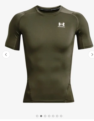 Grön tight t-shirt från Under Armour - Sportig grön t-shirt från Under Armour med korta ärmar och vit logga på bröstet. Modellen är tight och tillverkad i ett stretchigt syntetmaterial som andas, perfekt för träning. Snygg passform som framhäver axlar och armar.
