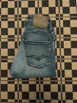 Replay Anbass blå jeans, W30 L32 - Säljer ett par Replay Anbass jeans i klassisk blå tvätt med snyggt slitna detaljer. Modellen har raka ben och fem fickor, samt Replay-logga på bakfickan. Jeansen är tillverkade i stretchig bomullsmix för extra komfort och har normal passform.