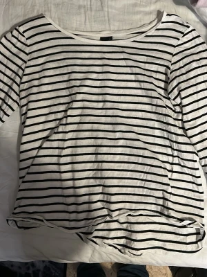 Randig långärmad topp Gina Tricot - Säljer en vit långärmad topp från Gina Tricot med svarta horisontella ränder. Toppen har en rund halsringning och är gjord i mjuk bomull, perfekt för en enkel och stilren look.