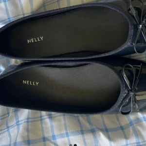Mörkblå ballerinaskor från Nelly - Snygga mörkblå ballerinaskor från Nelly med rund tå och dekorativ rosett framtill. Skorna har en glansig finish och är perfekta för en stilren look. Passar till både jeans och klänning.