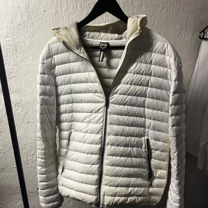Vit dunjacka från Colmar, strl 50 - Säljer en stilren vit dunjacka från Colmar i storlek 50. Jackan är lätt, har horisontella quiltade sömmar, dragkedja framtill och två fickor med dragkedja. Perfekt för kyliga dagar och har en clean look med diskret logga på ärmen.