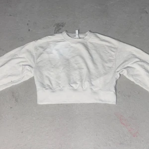 Vit croppad sweatshirt från H&M - En basic vit croppad sweatshirt från H&M med rund halsringning och långa ärmar. Tröjan är i mjuk bomullsmix och har bred mudd nertill för en snygg passform. Perfekt till jeans eller kjol för en clean och enkel look.