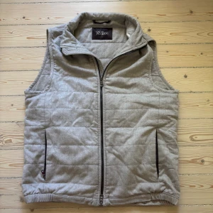 Beige quiltad väst Oscar Jacobson - Snygg beige quiltad väst från Oscar Jacobson med hög krage och dragkedja framtill. Västen har två fickor med dragkedja och diskreta knappar i nederkant bak. Skick 9/10 Inga defekter eller slitningar nypris cirka 3000 mitt pris 1599