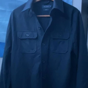 Mörkblå overshirt från Riley slim fit - Stilren mörkblå overshirt från Riley i slim fit-modell. Overshirten är i st S men passar som M. Den är i mycket bra skick och har inga defekter. Ny pris ligger runt 1500. Hör av dig vid minsta fundering🙌🙌