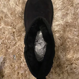 Svarta boots i mocka med platt sula - Helt oanvända UGGs i klassisk svart färg, beställda från Nelly. Supermjuka och varma, perfekta för höst och vinter. Passar dig som vill ha både stil och komfort i ett par skor.