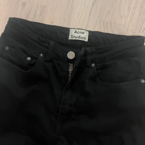 Svarta jeans från Acne Studios - Svarta jeans från Acne Studios med klassisk femficksdesign och dragkedja. Modellen är tight och har smala ben, perfekt för en clean och stilren look. Byxorna är i stretchigt bomullsmaterial och har normal midja.