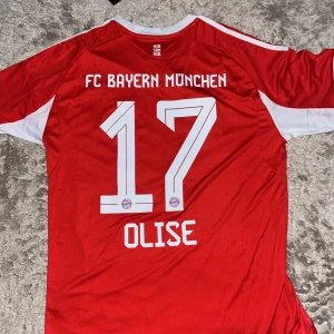 FC Bayern München matchtröja Adidas L - Säljer en officiell FC Bayern München fotbollströja från Adidas i storlek L. Tröjan är röd med vita detaljer, har korta ärmar och klubbmärke på bröstet. Nummer 17 och namnet Olise på ryggen. Tillverkad i lätt och ventilerande polyester.