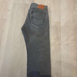 Grå Levi's 501 jeans straight fit - Säljer ett par grå Levi's 501 jeans med klassisk straight fit och femficksdesign. Jeansen har den ikoniska läderpatchen bak i midjan och röda Levi's-tag på bakfickan. Tillverkade i slitstarkt denimtyg och passar perfekt till en avslappnad stil.