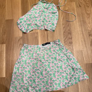 Blommig halterneck topp från Zara - Supersöt halterneck topp från Zara i blommigt mönster med rosa, gröna och gula toner. Toppen har smala knytband i nacken och är ärmlös, perfekt för varma dagar. Materialet känns lätt och luftigt, och mönstret ger en riktigt somrig vibe.