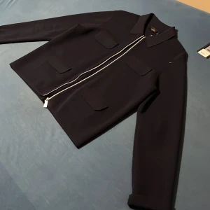 Morris Lady blå stickad overshirt L - Snygg mörkblå stickad overshirt från Morris Lady i storlek L. Jackan har fyra fickor framtill, klassisk krage och silverfärgad dragkedja. Perfekt för dig som gillar stilrena och tidlösa plagg med en modern twist.