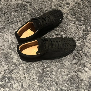 Christian Louboutin svarta sneakers med nitar - Svarta sneakers från Christian Louboutin i mocka med svarta nitar över tån och klassisk röd sula. Skorna har snörning och en stilren. Kommer med orginal dustbag. Säljes för att storleken var för liten