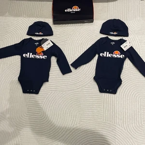 Ellesse baby set 12-18 mån nytt med tagg - Ellesse baby set i mörkblått body + mössa. Storlek: 12-18 månader. Helt nya, med taggar kvar och originalförpackning.