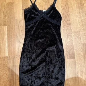 Svart sammetsklänning med spets H&M XS - Supersöt svart sammetsklänning från H&M i storlek XS. Klänningen har smala axelband, spetsdetaljer vid urringningen och en liten rosett framtill. Mjuk och glansig yta som ger en lyxig känsla. Perfekt för dig som gillar en feminin och trendig stil.